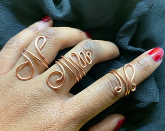 May include: Three copper wire rings with unique designs. The rings are worn on the fingers of a hand.
