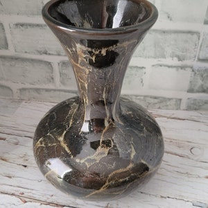 May include: A decorative vase with a glossy, dark brown finish and a unique marbled pattern in shades of gold and cream. The vase has a rounded base and a flared, trumpet-shaped top. The ceramic vase is suitable for home decor.