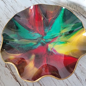 May include: A decorative bowl with a wavy edge and a gold rim. The interior features a vibrant abstract design with swirls of red, green, yellow, and brown. The bowl is likely made of resin or a similar material.