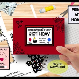 May include: A red birthday card with the text "Open When It's Your Birthday" and a black border. The card features a balloon, party hat, and hearts. Additional cards and stationery are visible.