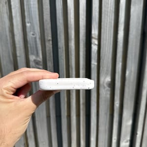 May include: A rectangular white ceramic object with a speckled pattern featuring small black dots across its surface. The object has rounded edges and a smooth, matte finish, presented in a horizontal orientation with a visible thickness.