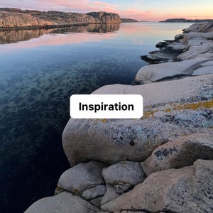 May include: A coastal landscape featuring large, smooth, light brown granite rocks in the foreground and a calm, dark blue body of water reflecting a soft pink and orange sunset sky. A white rectangular sign with the black text Inspiration.