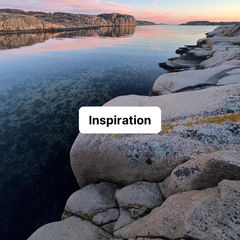 May include: A coastal landscape featuring large, smooth, light brown granite rocks in the foreground and a calm, dark blue body of water reflecting a soft pink and orange sunset sky. A white rectangular sign with the black text Inspiration.