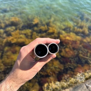 K&ouml;nnte beinhalten: Ein Paar zylindrische Metallrohre mit silberfarbener Au&szlig;enseite und glattem, dunklem Innenraum. Die beiden R&ouml;hren sind miteinander verbunden und weisen eine gr&ouml;&szlig;ere kreisf&ouml;rmige &Ouml;ffnung neben einer kleineren &Ouml;ffnung auf, von oben betrachtet.
