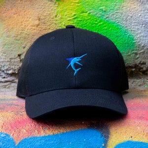 Peut inclure: Une casquette de baseball noire avec un filet à l'arrière et un marlin bleu et blanc brodé sur le devant.