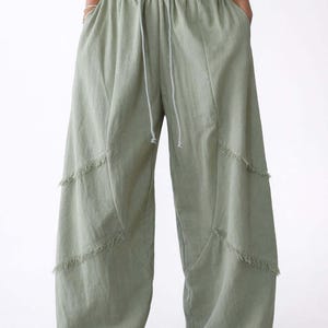 May include: Sage green wide-leg pants with a drawstring waist and fringe detailing. The pants have a relaxed fit and are made of a lightweight fabric. The pants are a solid color and have a casual style.