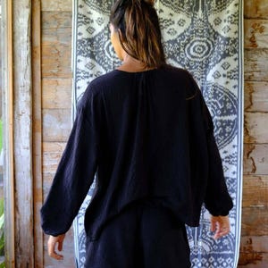 Back view of Night Long Sleeve Cardigan in deep navy — oversized batwing sleeve silhouette, soft cotton gauze drape, styled as a matching co-ord set with black cotton shorts against boho ikat backdrop