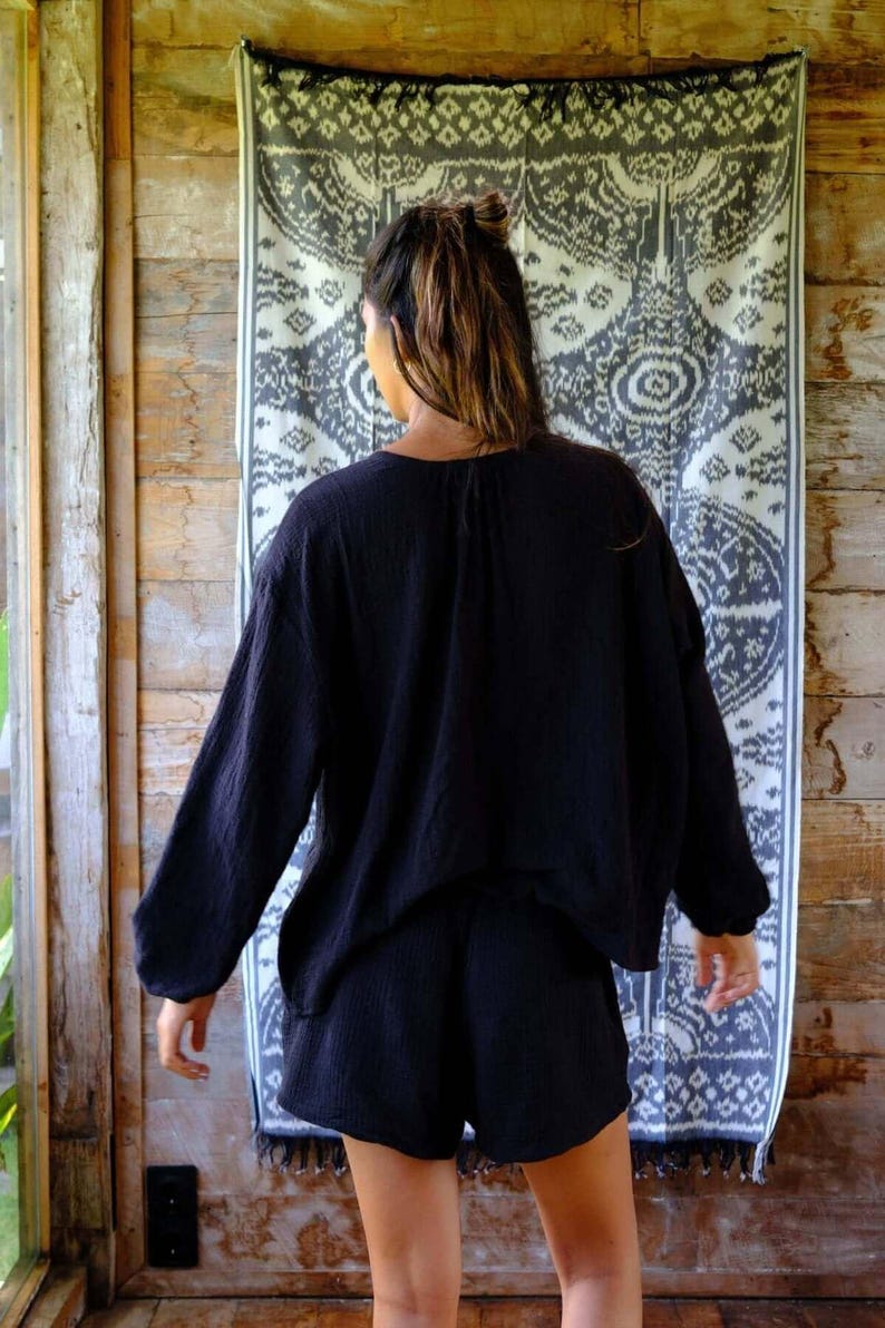 Back view of Night Long Sleeve Cardigan in deep navy — oversized batwing sleeve silhouette, soft cotton gauze drape, styled as a matching co-ord set with black cotton shorts against boho ikat backdrop