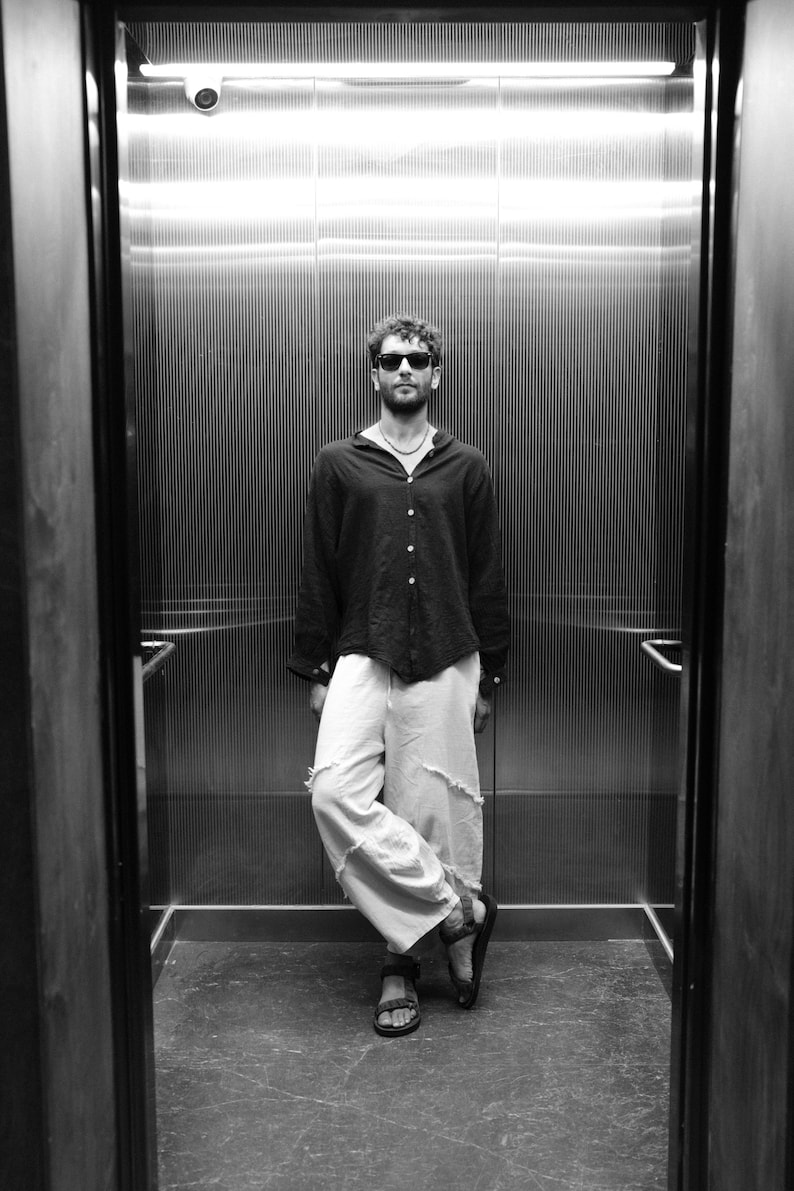 Man styling the black boho shirt with wide-leg trousers for an urban nomad look.