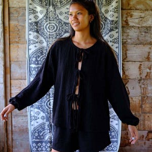 Full-length front view of Night Long Sleeve Cardigan styled as a complete black cotton co-ord — cheerful model showing all four bow tie front closures open, relaxed oversized fit paired with matching cotton shorts