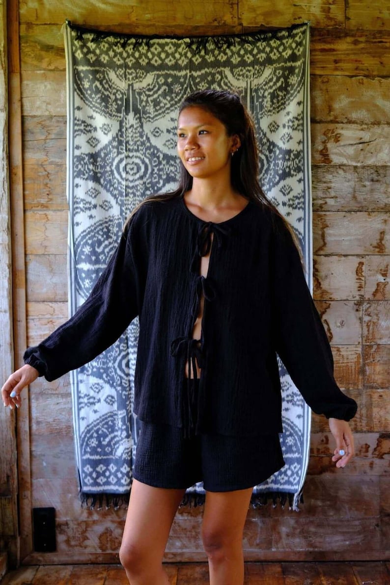 Full-length front view of Night Long Sleeve Cardigan styled as a complete black cotton co-ord — cheerful model showing all four bow tie front closures open, relaxed oversized fit paired with matching cotton shorts