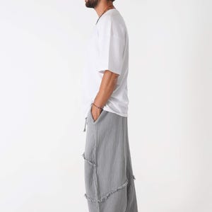 Handmade linen palazzo pants in light gray with tiered, frayed seams, worn by a male model in a white tee (boho yoga trousers).