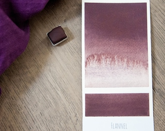 May include: A watercolor paint swatch card with a gradient of brown and purple shades. The card is labeled "FLANNEL".
