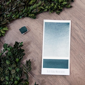 May include: A watercolor paint swatch card with a gradient of blue and green shades. The card is labeled "Blue Ridge Mountains".