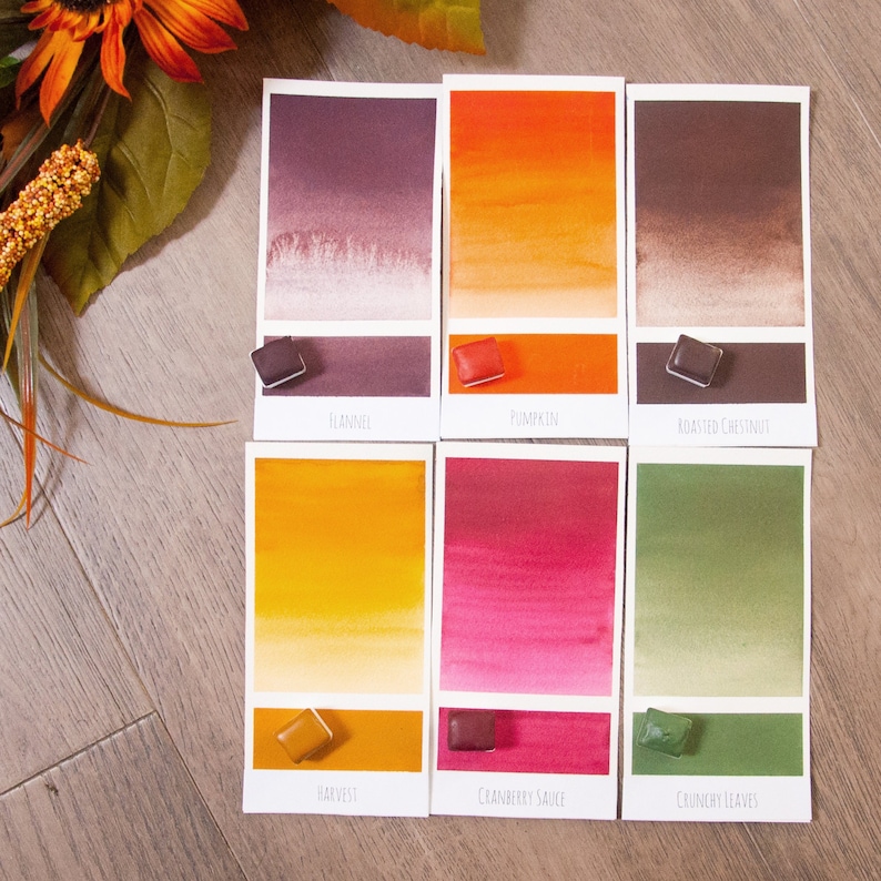 May include: Six watercolor paint swatches with names "Flannel", "Pumpkin", "Roasted Chestnut", "Harvest", "Cranberry Sauce", and "Crunchy Leaves". Each swatch shows a gradient of color from light to dark.