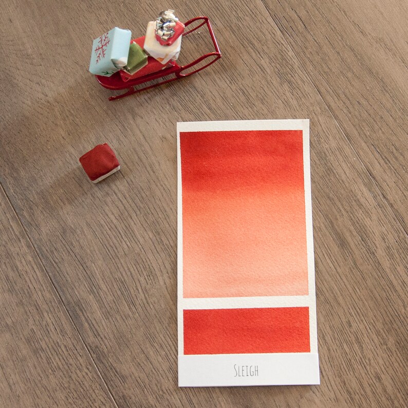 May include: A watercolor paint swatch card with a gradient of red and orange colors. The card is labeled "SLEIGH".