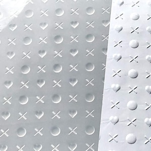 Könnte beinhalten: Ein weißes Blatt Papier mit einem sich wiederholenden Muster aus Kreisen, Herzen und Xs. Das Muster ist geprägt und erzeugt eine erhabene Textur.