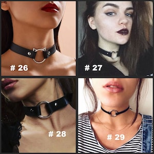 May include: Four different black choker necklaces with silver accents. The first choker has a cat-shaped charm, the second has a heart-shaped charm, the third has a large round ring, and the fourth has a smaller round ring.