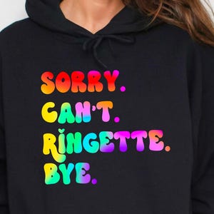 May include: A black hoodie with a rainbow-colored graphic that says "SORRY. CAN'T. RINGETTE. BYE."