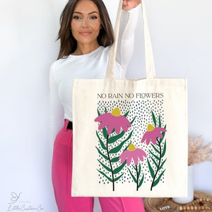 Może przedstawiać: Biała torba typu tote z wzorem r&oacute;żowych kwiat&oacute;w i tekstem "NO RAIN NO FLOWERS".