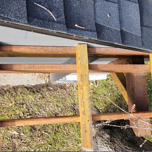 May include: A close-up view of a wooden frame being constructed against a gray wall. The frame is made of brown and yellow wood and is being built against a gray wall with a black roof.