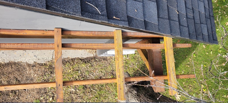 May include: A close-up view of a wooden frame being constructed against a gray wall. The frame is made of brown and yellow wood and is being built against a gray wall with a black roof.