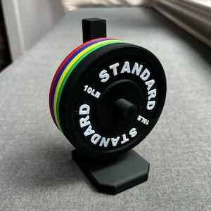May include: A black 10lb weight plate with a black stand. The plate has a white "STANDARD" inscription and a red, yellow, green, and blue color band.