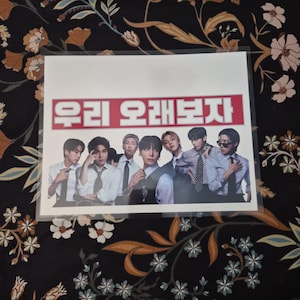 May include: A printed image featuring a group of seven people in formal attire. The image has Korean text in a red rectangle at the top. The background is a dark floral pattern.