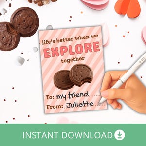 Puede incluir: Una tarjeta de San Valentín con el texto "life's better when we EXPLORE together." La tarjeta presenta dos galletas de chocolate y espacio para escribir "To: my friend" y "From: Juliette." La imagen incluye corazones de papel y un bolígrafo.