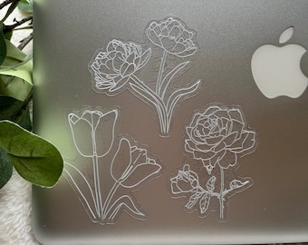 Könnte beinhalten: Vier weiße Umriss-Blumenaufkleber auf einem silbernen Laptop. Die Aufkleber zeigen eine Rose, zwei Tulpen und eine Pfingstrose.