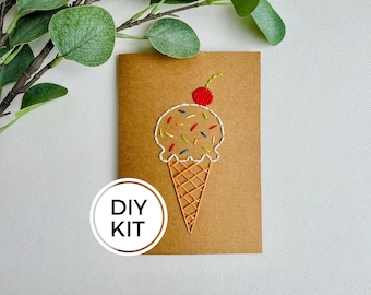 May include: DIY kit for creating a brown card with an embroidered ice cream cone design. The ice cream is white with colorful sprinkles and a red cherry on top. The cone is orange and white.