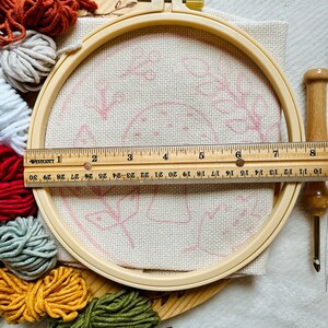 Mushroom foliage punch needle embroidery kit showing kit components including printed fabric with no-slip hoop, colored yarn. Punch Needle tool with threader example. Ruler Showing hoop size about 8 inches.
