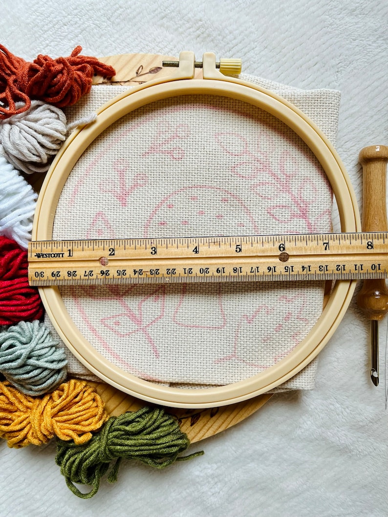 Mushroom foliage punch needle embroidery kit showing kit components including printed fabric with no-slip hoop, colored yarn. Punch Needle tool with threader example. Ruler Showing hoop size about 8 inches.