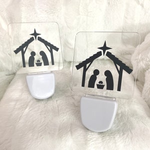 May include: Two white plug-in night lights with clear plastic covers featuring a black silhouette of the nativity scene with a star above the stable.