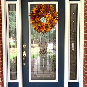 May include: A blue front door with a white frame and a fall-themed wreath made of orange, yellow, and brown leaves.