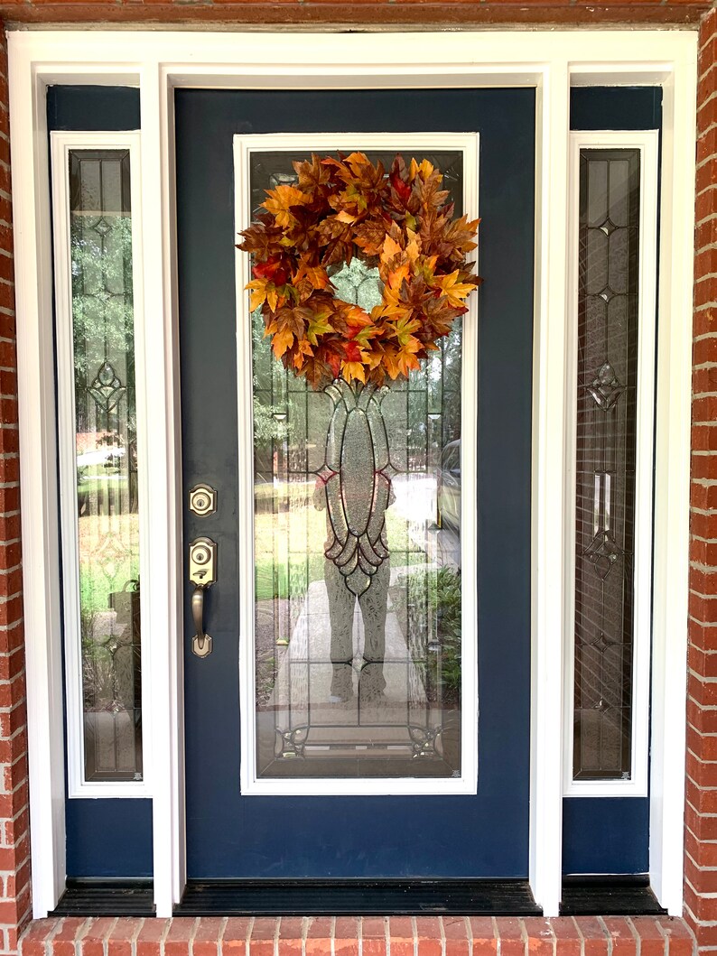 May include: A blue front door with a white frame and a fall-themed wreath made of orange, yellow, and brown leaves.