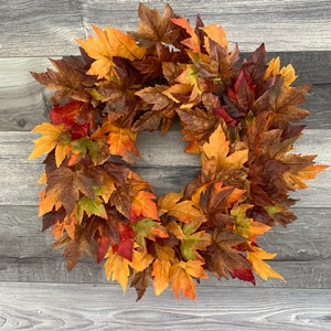 May include: A fall-themed wreath made of artificial maple leaves in shades of orange, red, brown, and yellow.