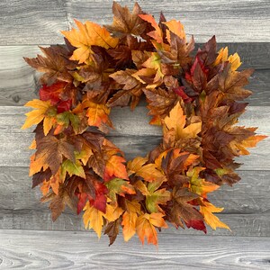 May include: A fall-themed wreath made of artificial maple leaves in shades of orange, yellow, red, and brown.