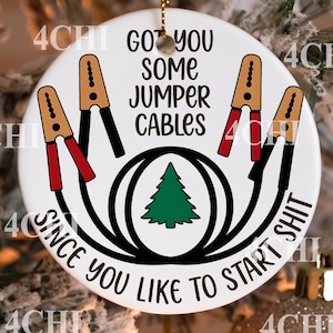 May include: A white ceramic Christmas ornament with the text "GOT YOU SOME JUMPER CABLES SINCE YOU LIKE TO START SHIT". The ornament features illustrations of jumper cables and a green Christmas tree.
