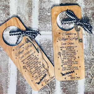 May include: Two wooden door hangers with a keyhole and a small key attached. Each hanger has a message that reads "Santa's Magic Key" and is addressed to a different person. The message includes a rhyme about the key only working on Christmas Eve.