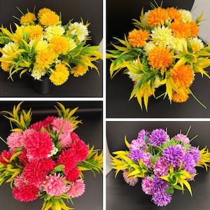 May include: A collection of four artificial flower arrangements featuring spherical blooms in yellow, orange, pink, and purple. Each bouquet includes pointed, bright green foliage interspersed among the dense, textured flower heads.