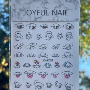 Op de afbeelding: Een vel met witte nagelstickers met verschillende schattige cartoon-hondendesigns. De stickers tonen honden met verschillende gezichtsuitdrukkingen, die harten, ballonnen en bloemen vasthouden. Het vel is gelabeld met "JOYFUL NAIL" en "JO-2230".