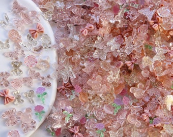 May include: A large assortment of pink and clear glitter resin charms. The charms include butterflies, bows, flowers, and Mickey Mouse heads.