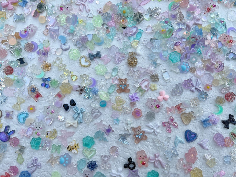 May include: Assortment of colorful resin charms in various shapes, including hearts, stars, butterflies, bows, and animals. The charms are translucent and have a sparkly finish.