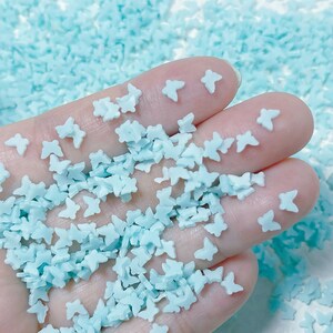 May include: A handful of light blue butterfly shaped sprinkles. The sprinkles are small and perfect for decorating cakes, cupcakes, and other desserts.