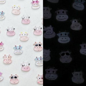 May include: A sheet of white paper with a variety of colorful cow stickers. The stickers are arranged in a grid pattern and are all facing the same direction. The stickers are glow-in-the-dark and have a black outline. The stickers are all different colors, including pink, blue, yellow, and green.