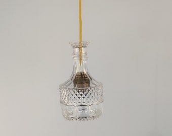 May include: A clear glass pendant light fixture shaped like a decanter with a gold metal ceiling mount and a yellow cord.