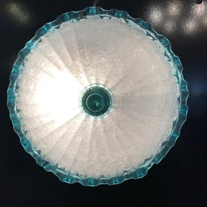 May include: A white, ruffled lampshade with a light blue trim. The lampshade is illuminated from within, casting a soft glow.