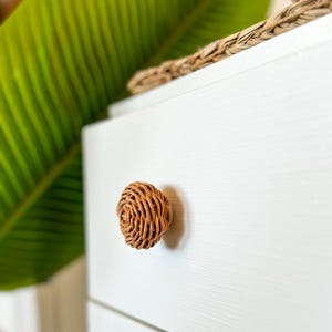 May include: A white drawer with a woven wicker knob. The drawer is part of a dresser or cabinet.