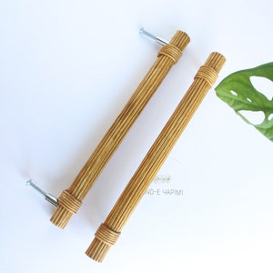 May include: Two natural woven rattan cabinet pulls with silver screws. The pulls are approximately 15 cm long.